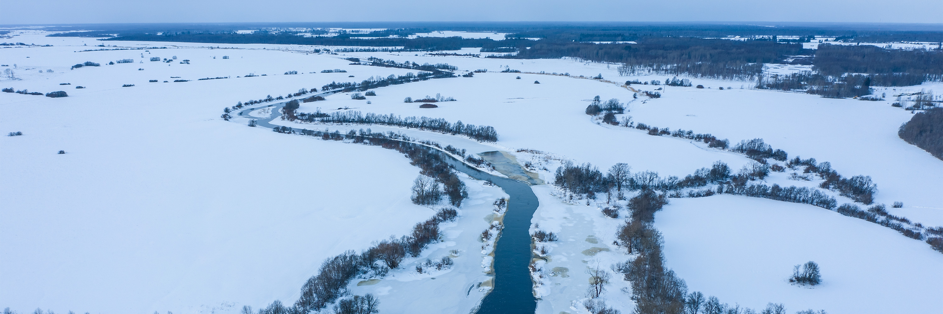 Drooni vaade talvisele Kasari jõele ja lumisele luhale (lage maa-ala, jõe ääres on puud)