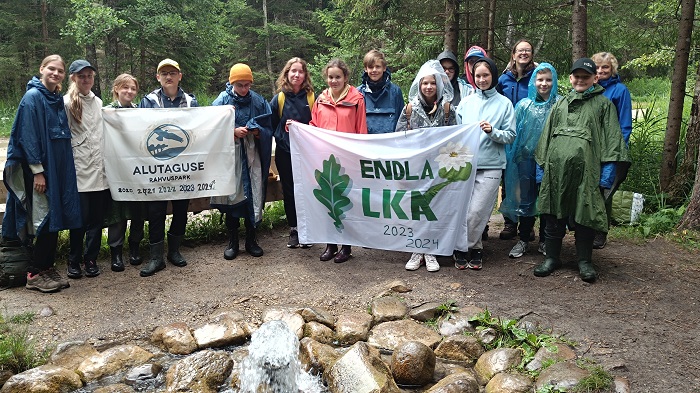 grupipilt noorte looduskaitskjatega, kes seisavad purskava allika juures, käes Endla ja Alutaguse logodega  lipud