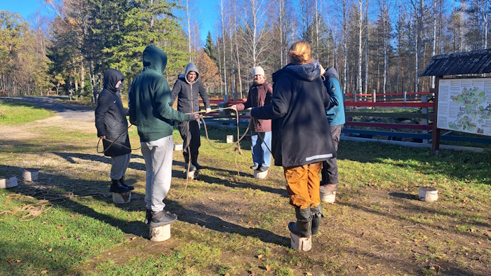 Pildil on noored koos Tipu looduskooli juhendajaga mängimas meeskonnamängu, seistes pakkudel ja hoides käes nööri ringis.