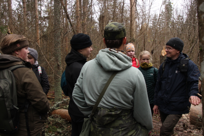 rühm inimesi seismas metsas mahalangenud puutüve juures ja arutlemas