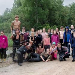 kolmkümmend inimest seisab tiigi servas, riided mudaga koos, aga nägu rõõmus