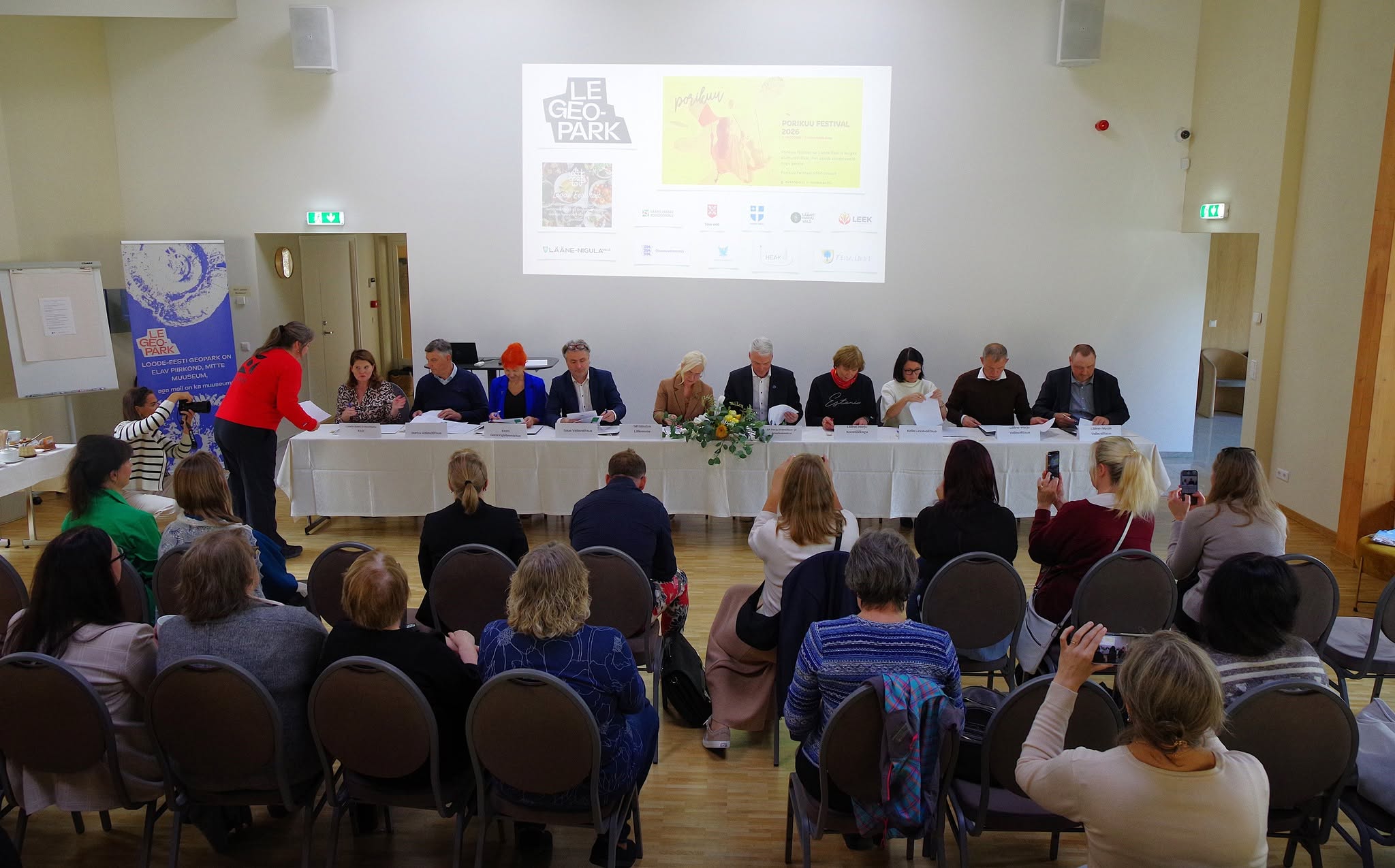 Inimesed istuvad valge laua taga ja allkirjastavad dokumente